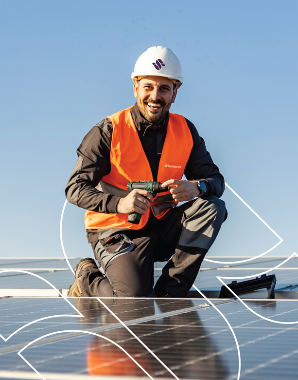 Solar PV Engineer, kneeling next to solar panels, wearing workwear and an orange high viz jacket and white hard hat.